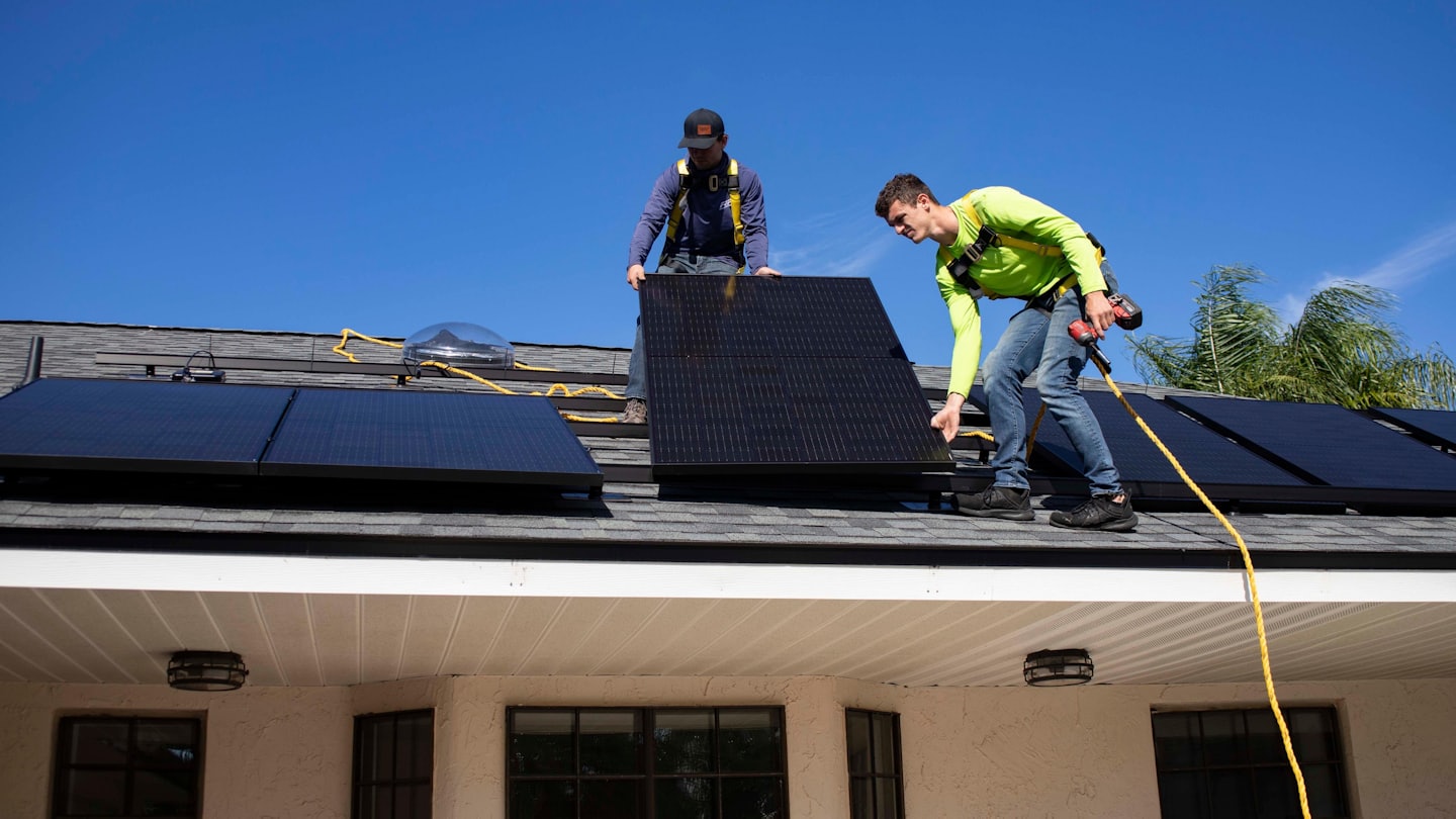 Des ouvriers installent des panneaux solaires sur le toit d'une maison.
